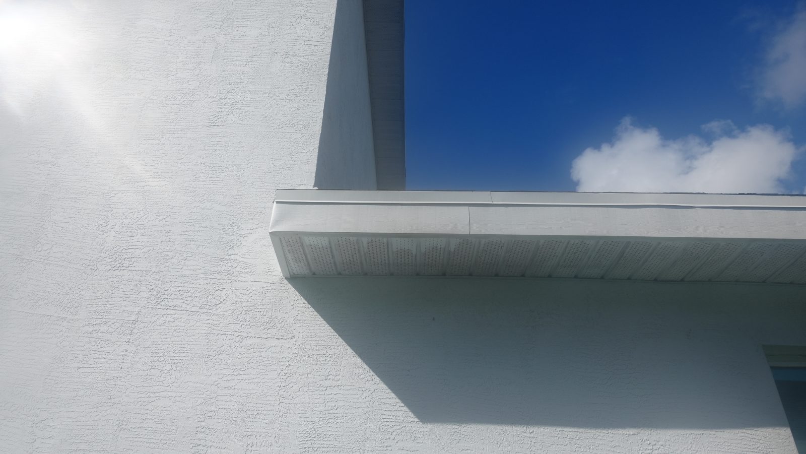 Two-story stucco wall meeting the one-story garage roof fascia and soffit; no gutter